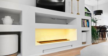 Custom great room storage with linear electric fireplace, TV mount, open shelves, gold lamps, and pl