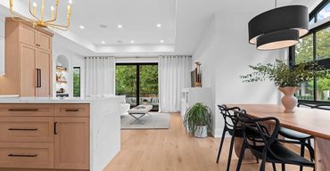 Bright open kitchen-great room with oak cabinets marble island, black dining chairs, gold chandelier