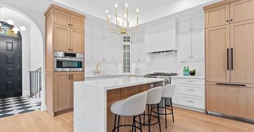 Luxury kitchen with waterfall marble island on oak base, white shaker cabinets, gold chandelier.