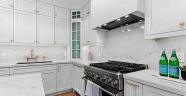Bright white shaker kitchen with 48" stainless range hood, marble backsplash, gold hardware, and pro