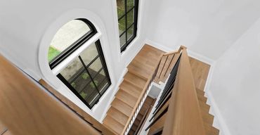 Elegant oak staircase with black iron balusters, oak handrail, white risers, and arched window overh