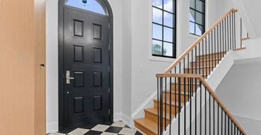 Elegant black front door with half-round transom window, sidelights, and white trim in bright foyer