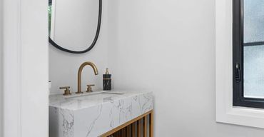 Luxurious powder room with white marble walls, deep vanity, vessel sink, frameless mirror, and black