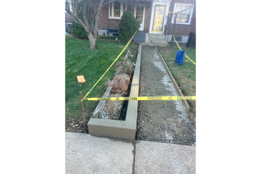 Sidewalk construction with caution tape around fresh concrete and a bordering planter box.