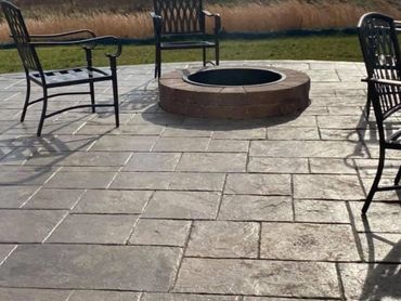 Outdoor patio with metal chairs around a brick fire pit on stone tiles.