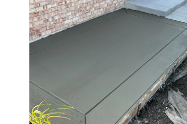 Freshly poured and smoothed concrete patio next to a brick wall.