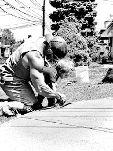 A man helps a child draw on the sidewalk outdoors.