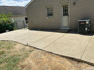 Freshly poured concrete patio outside a house with a back door and air conditioning unit.