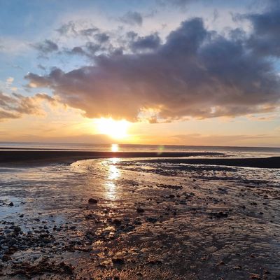 Sunset over a rocky beach with flowing water and dramatic clouds.