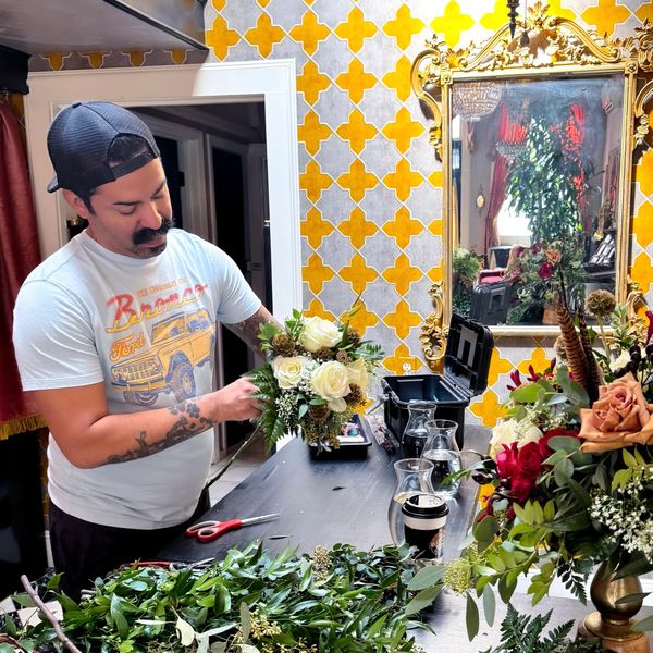 Man arranging white roses in a vibrant, decorated room.