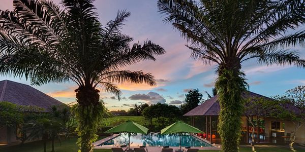 Sunset view of a tropical resort with pool and palm trees.