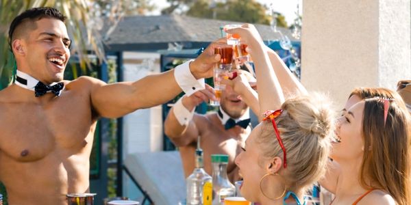 Friends in swimwear toasting with drinks at an outdoor pool party.