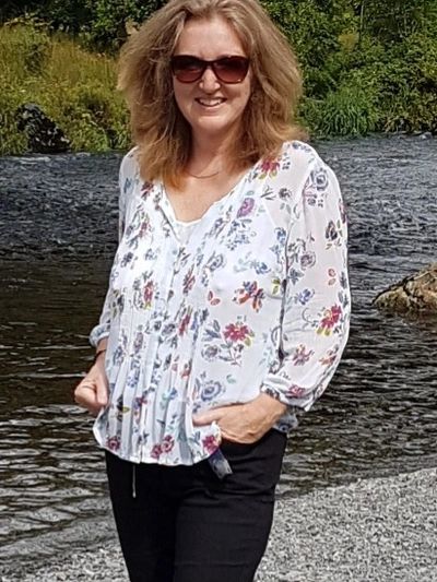 Woman in sunglasses standing by a river wearing a floral blouse.