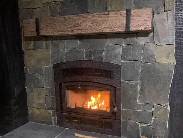 Stone fireplace with a wooden mantel and burning fire inside.