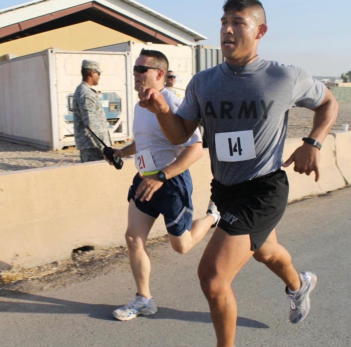 Two men in Army gear running a race outdoors under the sun.