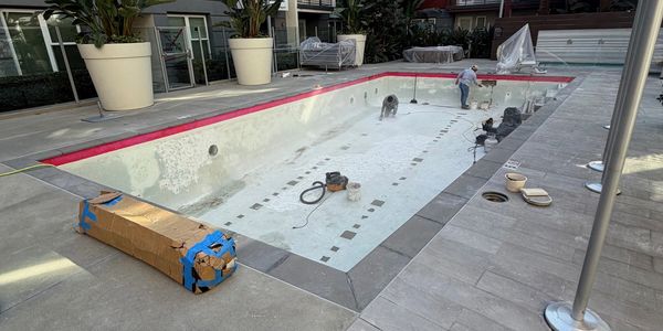 Workers renovating an empty swimming pool with tools around.
