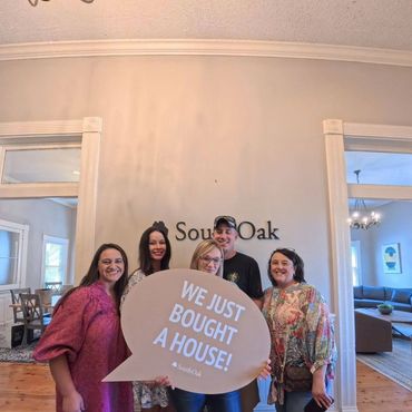 Happy group celebrating buying a house holding a sign that says 'We just bought a house!'