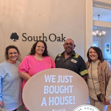 Four people smiling, holding a sign that says "We just bought a house!" at South Oak.