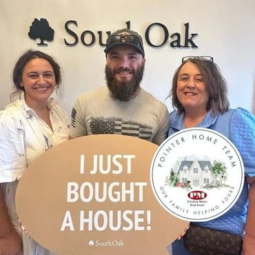 Three people smile holding a sign announcing a house purchase at South Oak.