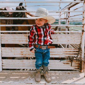 little cowboy standing on trailer in front of his horse