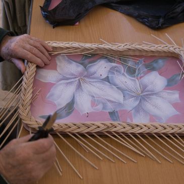 Hands weaving a wicker frame around a floral painting.