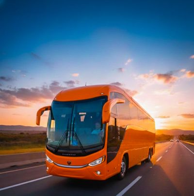 Bright orange bus driving on highway at sunset.