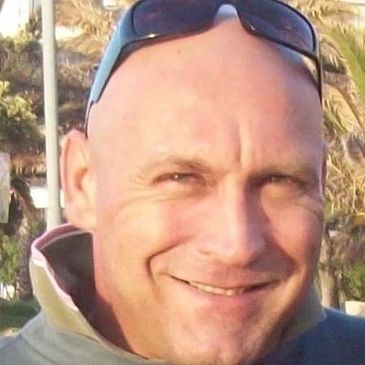 Smiling bald man wearing sunglasses on his head outdoors.