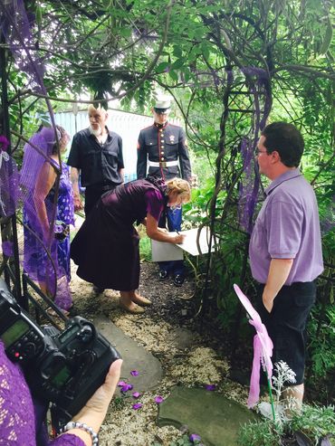 A group gathers under greenery with a Marine in uniform and our Senior Director signing a document.