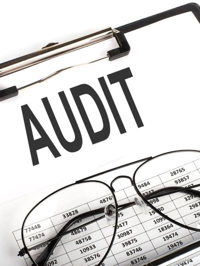 Clipboard with the word AUDIT and glasses on a financial document.