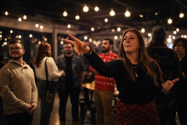 A woman playing darts with friends in a warmly lit room.