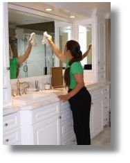 A woman cleaning a large bathroom mirror with a cloth.