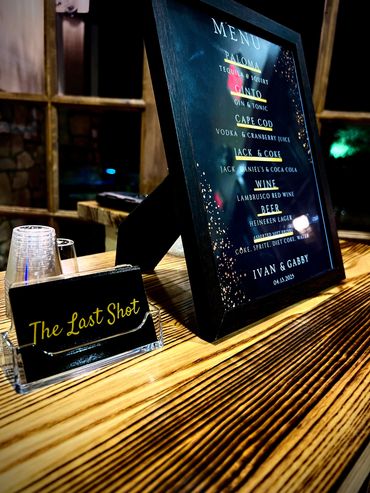 A framed drinks menu and a card holder on a wooden table.