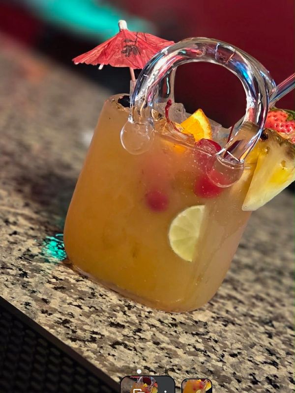 Tropical cocktail in a unique glass with a small umbrella and fruit garnishes.