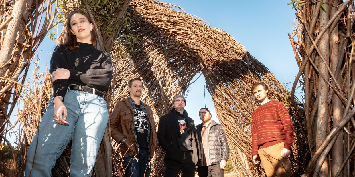 Group of five people posing outdoors with woven wood structures.