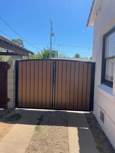 Brown vertical-infill side-yard gate in a black metal frame beside a stucco home