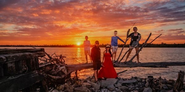 Group of five people posing by the lake during a vibrant sunset.