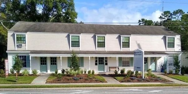 Two-story white building with green doors and windows under a clear blue sky.