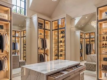 Luxurious walk-in closet with marble island and glass shelving.