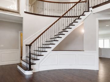 Elegant curved staircase with dark wood treads and wainscoting.