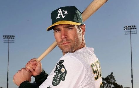 Baseball player in Oakland Athletics uniform posing with bat on field.