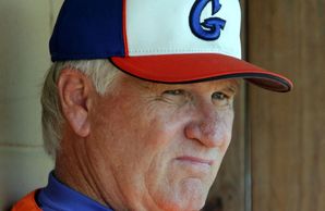 Elderly man in a colorful cap and orange jacket looking thoughtfully.