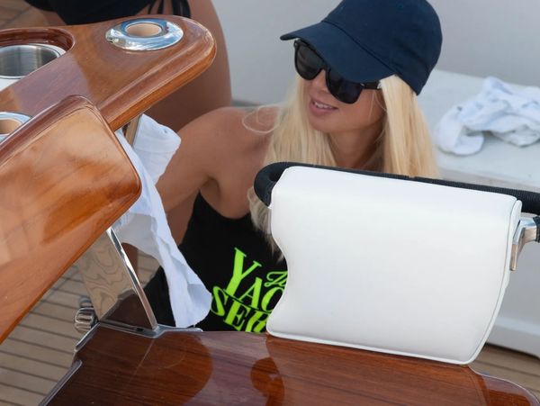Woman cleaning a wooden boat surface wearing sunglasses and a cap.