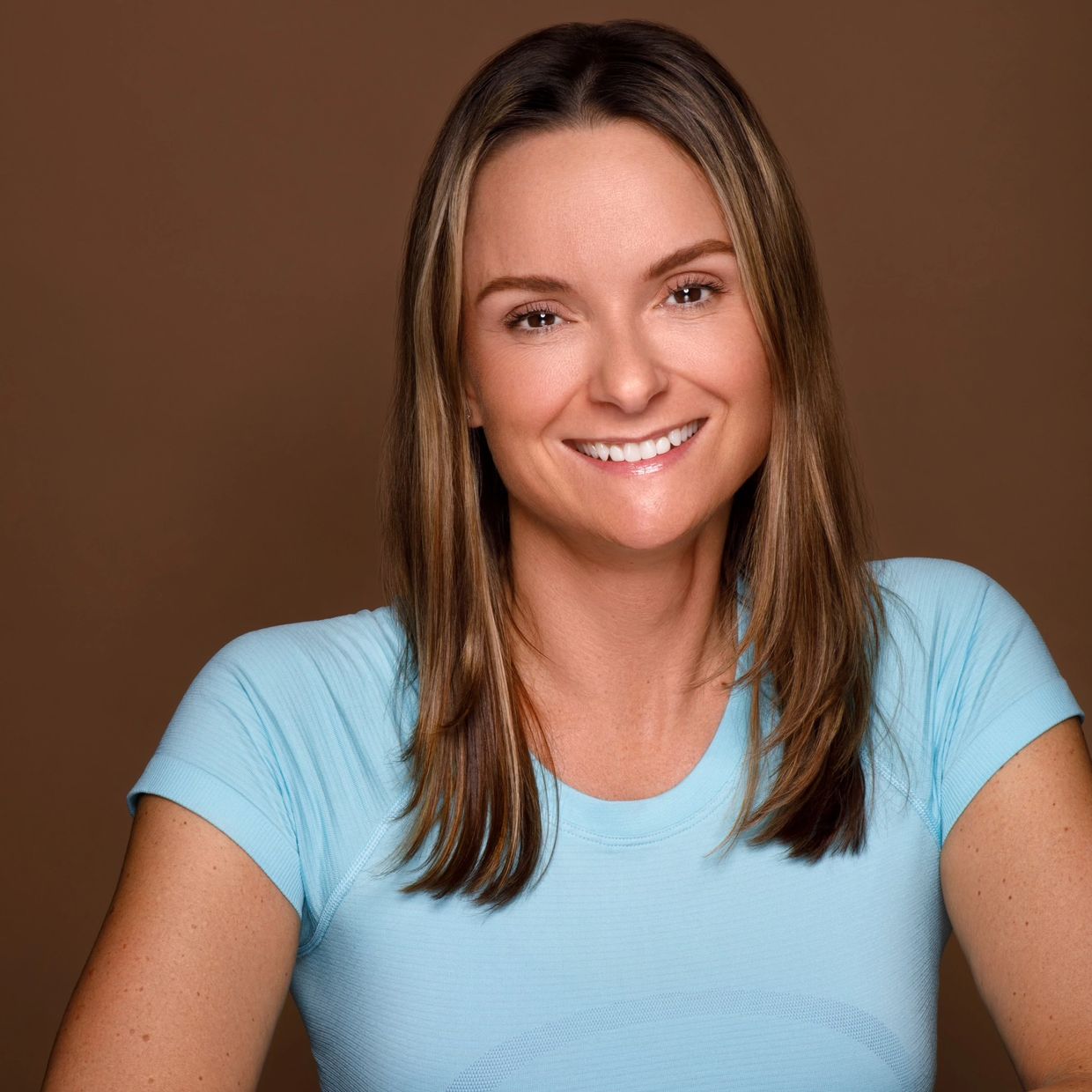 Smiling woman in a light blue shirt against brown background.