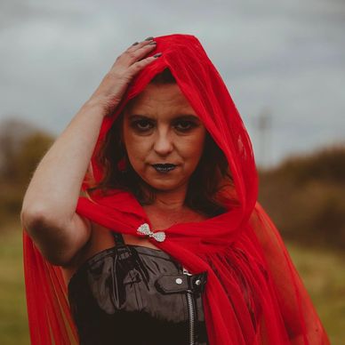 Woman in a red hooded cloak and dark lipstick.