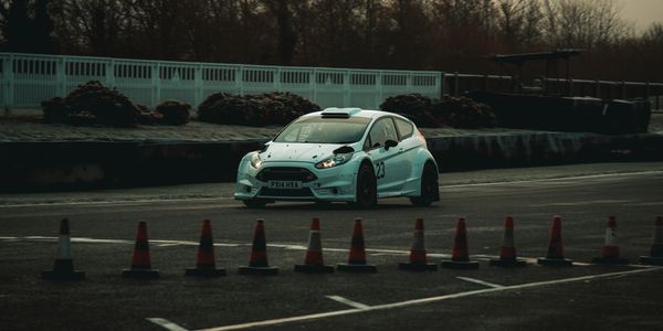 White rally car driving on a race track lined with cones.