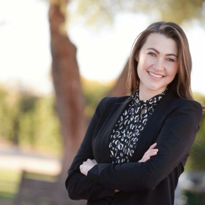 Smiling woman in business attire with arms crossed outdoors.
