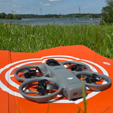 A gray DJI drone resting on an orange landing pad in a grassy field.