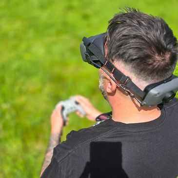 Man wearing VR goggles holding a controller outdoors on grass.