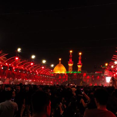 Night view of a golden-domed shrine with a large crowd and red lighting.