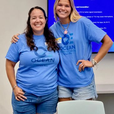 Two women smiling, wearing blue Ocean Conservancy shirts.